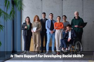 A diverse group of business people standing, including a man in a wheelchair. Text overlay "Is There Support For Developing Social Skills?"