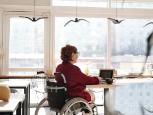 Person in a wheelchair working on a laptop in a bright, modern space, highlighting independent living with disability.