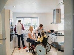 Family assisting a wheelchair user in the kitchen, illustrating the impact of specialised support coordination on well-being.