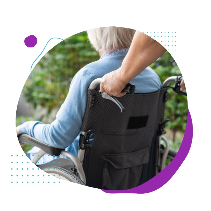 Aged care and disability support worker assisting an elderly woman in a wheelchair outdoors, providing compassionate care in a green, peaceful setting.